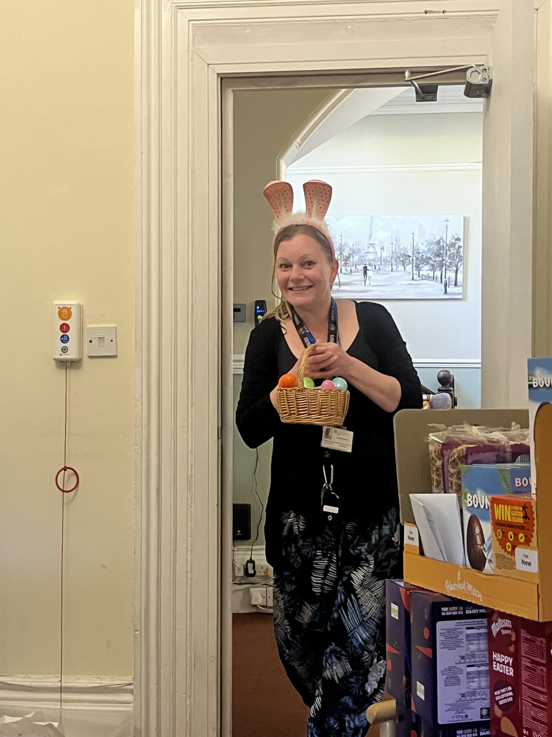 Carer Gemma dressed in bunny ears holding a basket of colourful plastic eggs scaled
