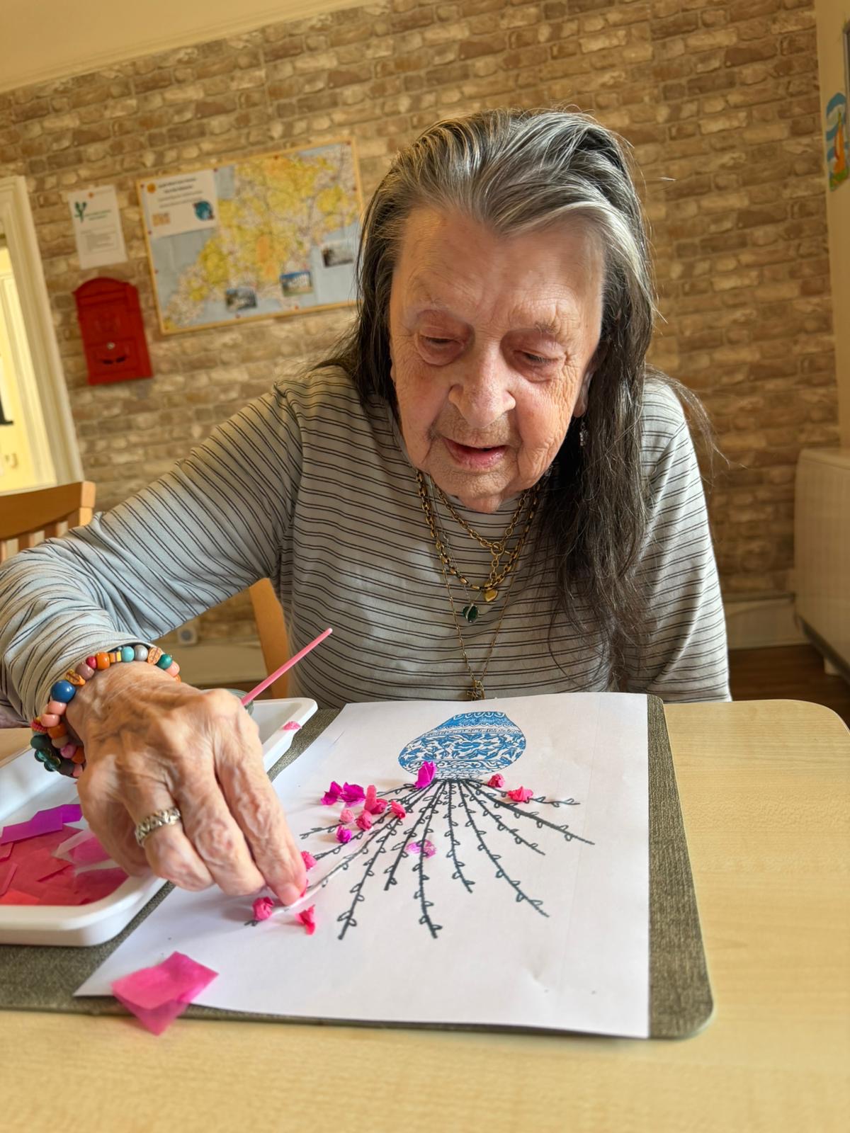 Female resident sticking tissue paper balls to a picture of a vase of stalks with PVA glue