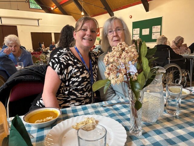 Female resident with carer enjoying soup rotated