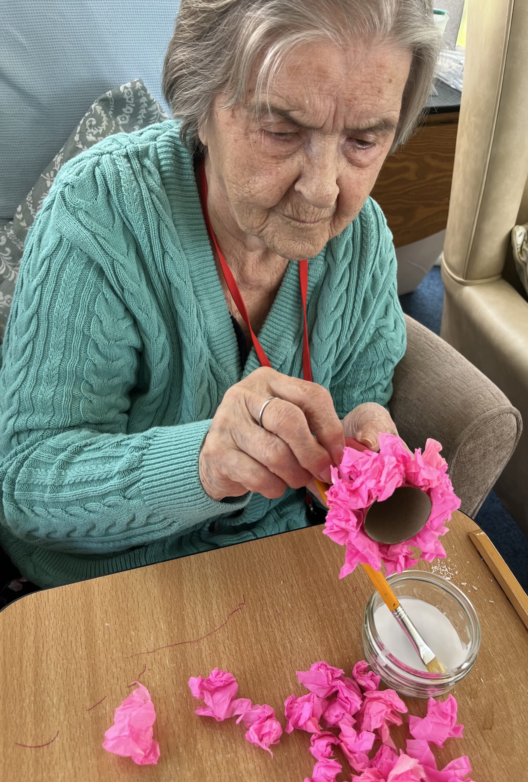 Herta enjoying gluing bright pink tissue paper petals to a cardboard roll scaled