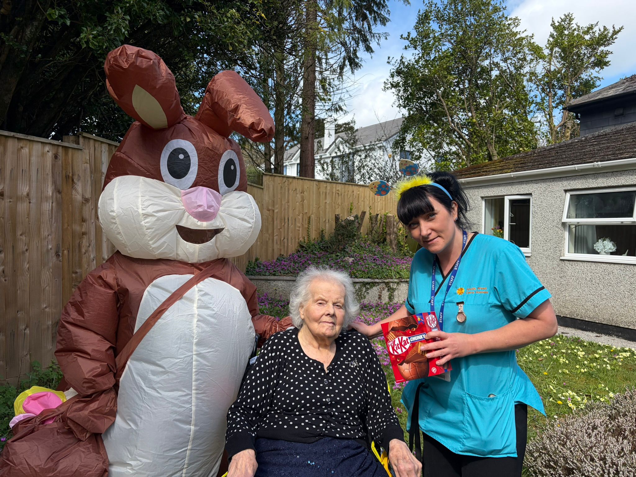 Resident and carer outside in the garden posing for a photo with the Easter bunny with an Easter egg