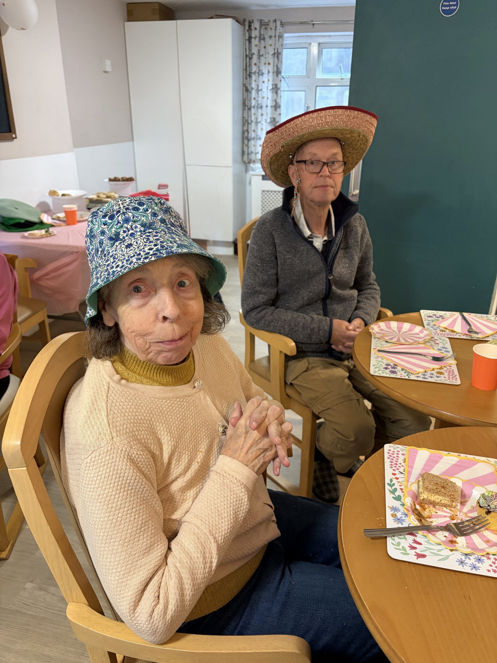 Residents seated around a table enjoying the party food wearing hats scaled