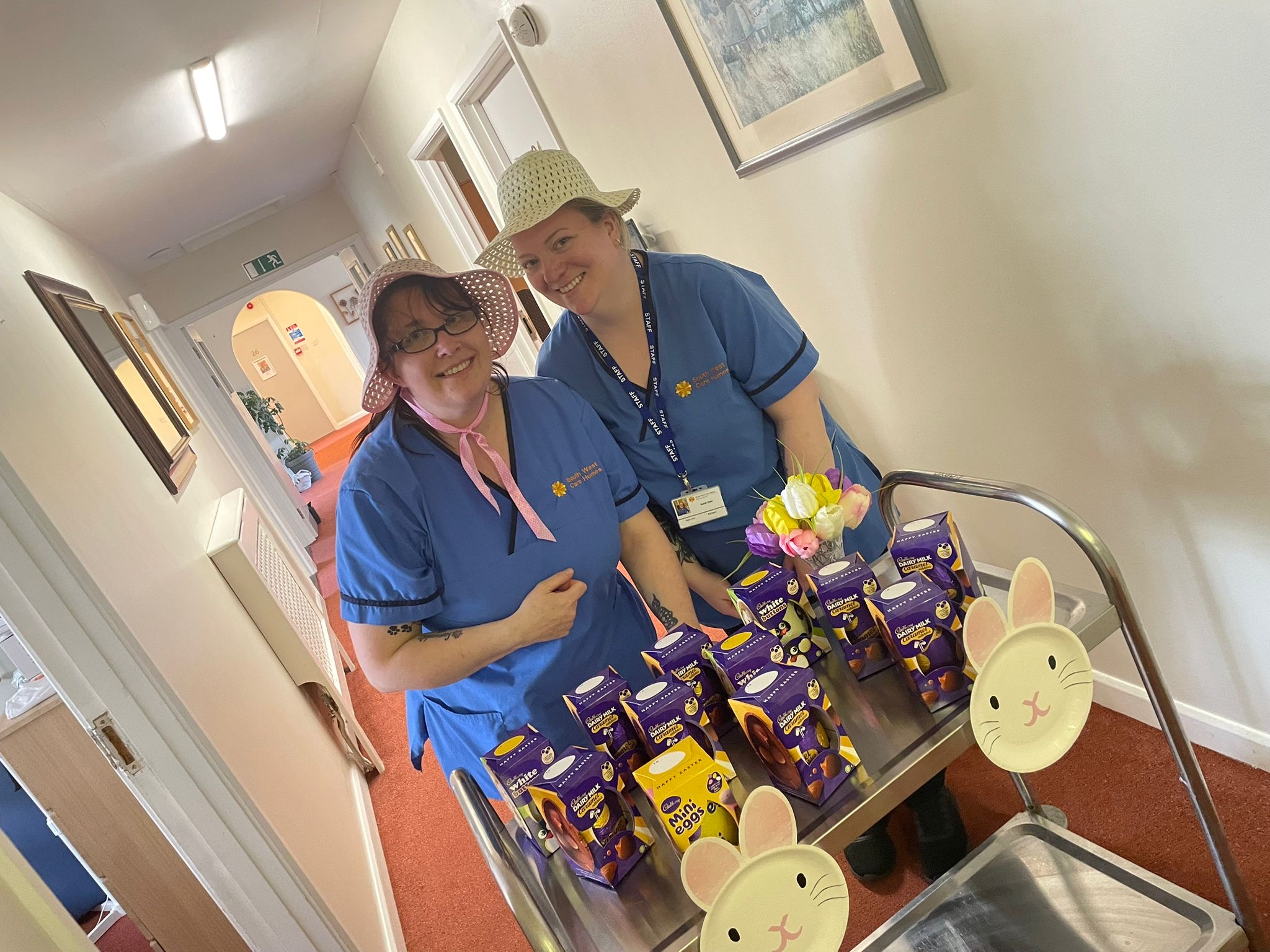 Sarah and Paula wearing Easter bonnets with a trolley filled with chocolate Easter eggs