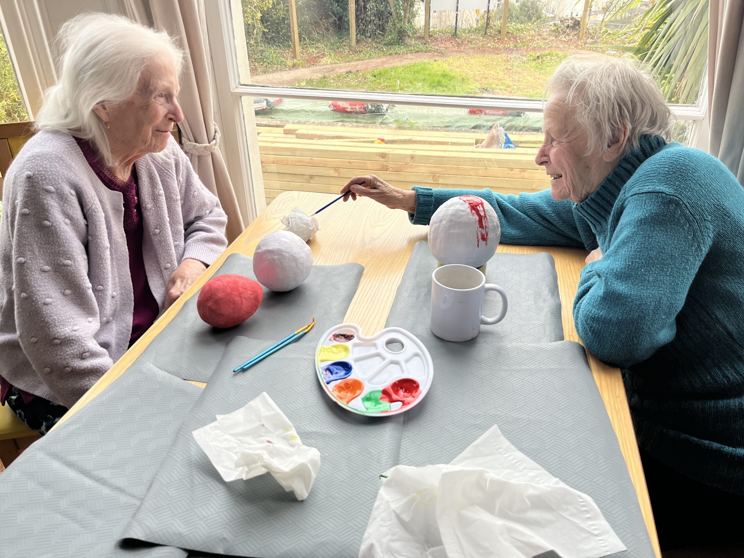 Two female residents painting their Easter eggs with chat and a cup of tea scaled