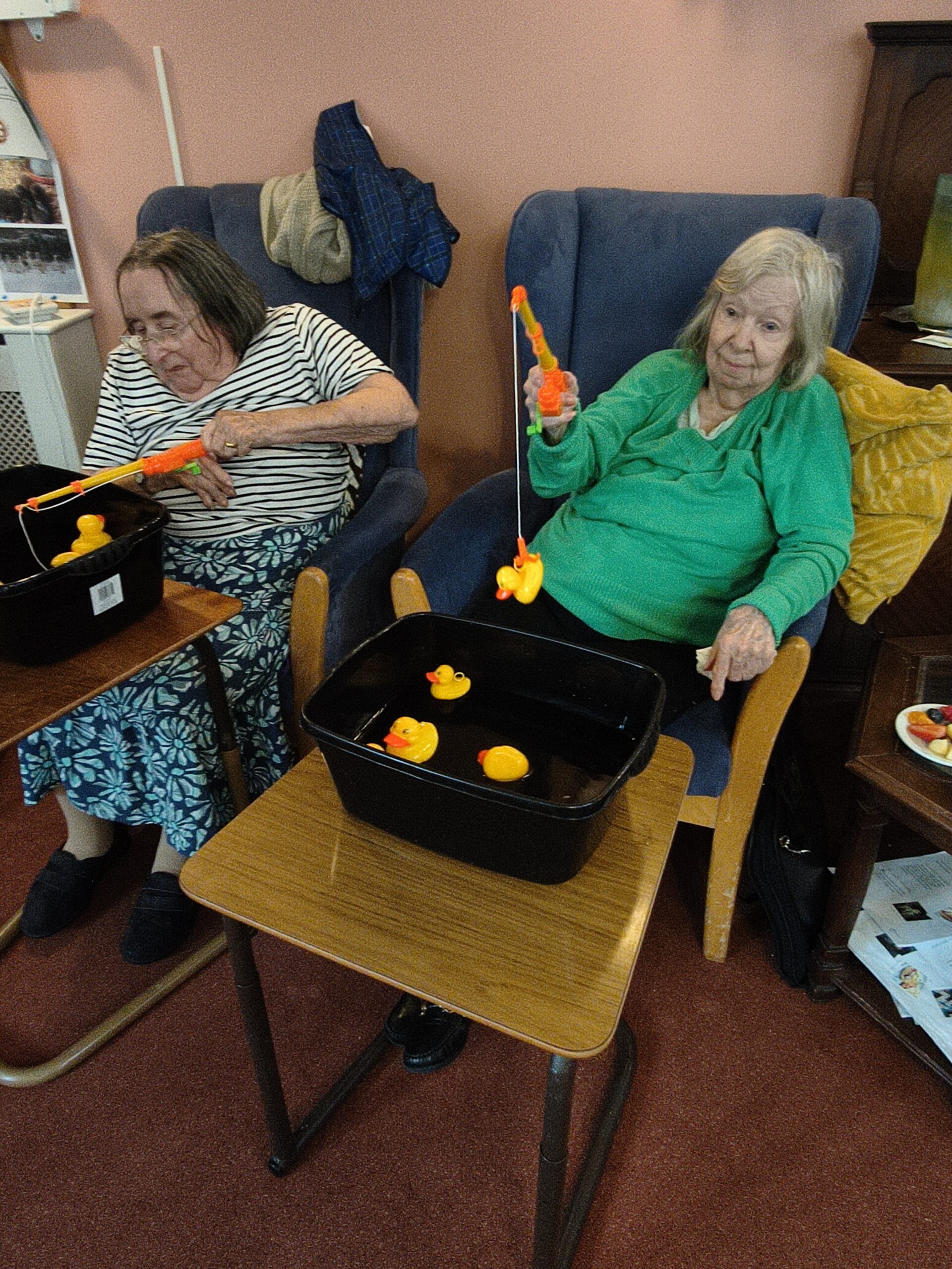 Two female residents sat together hooking ducks from the bowls in front of them scaled