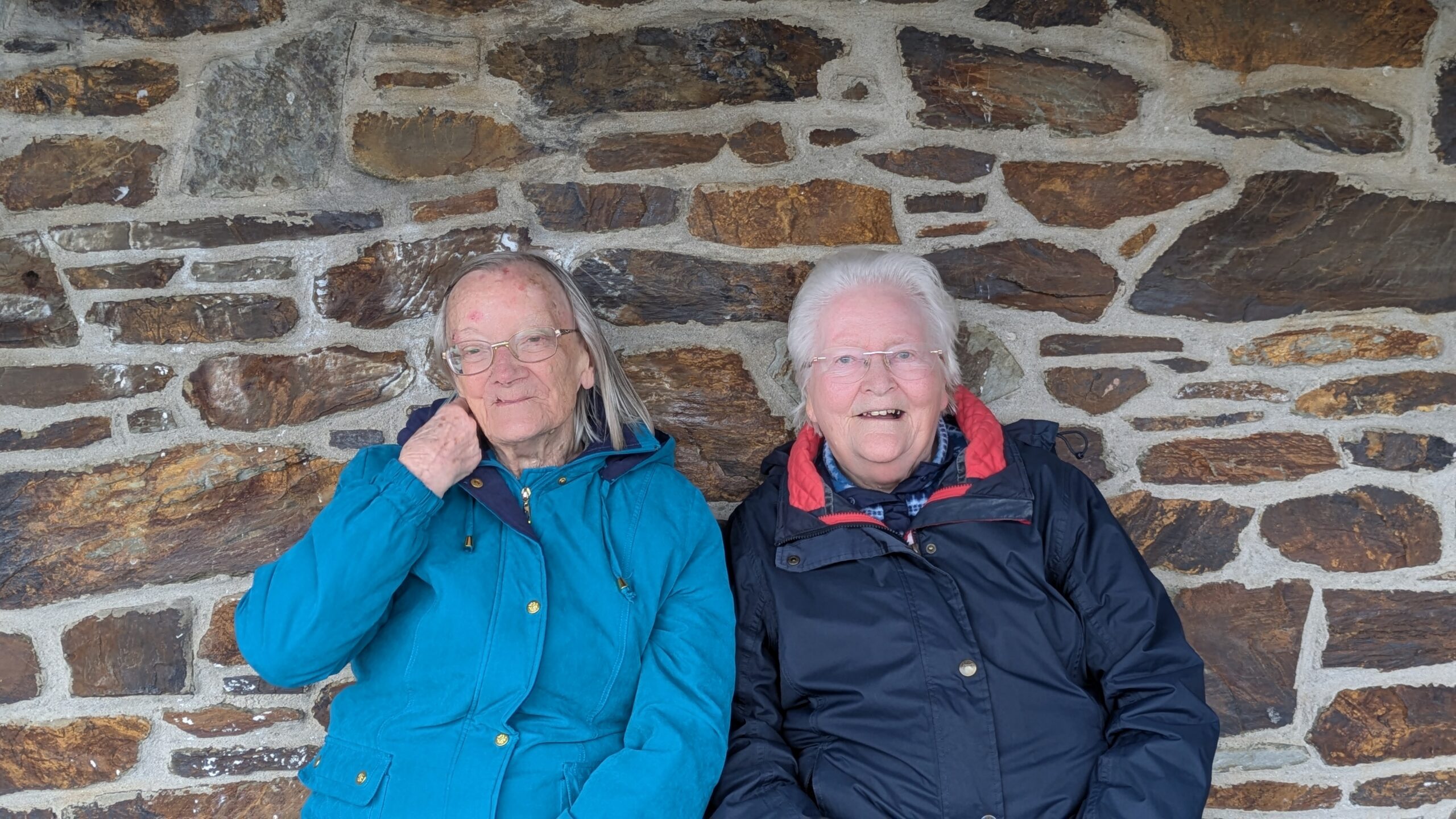 Two female residents wrapped up in warm coats sitting outside and smiling scaled