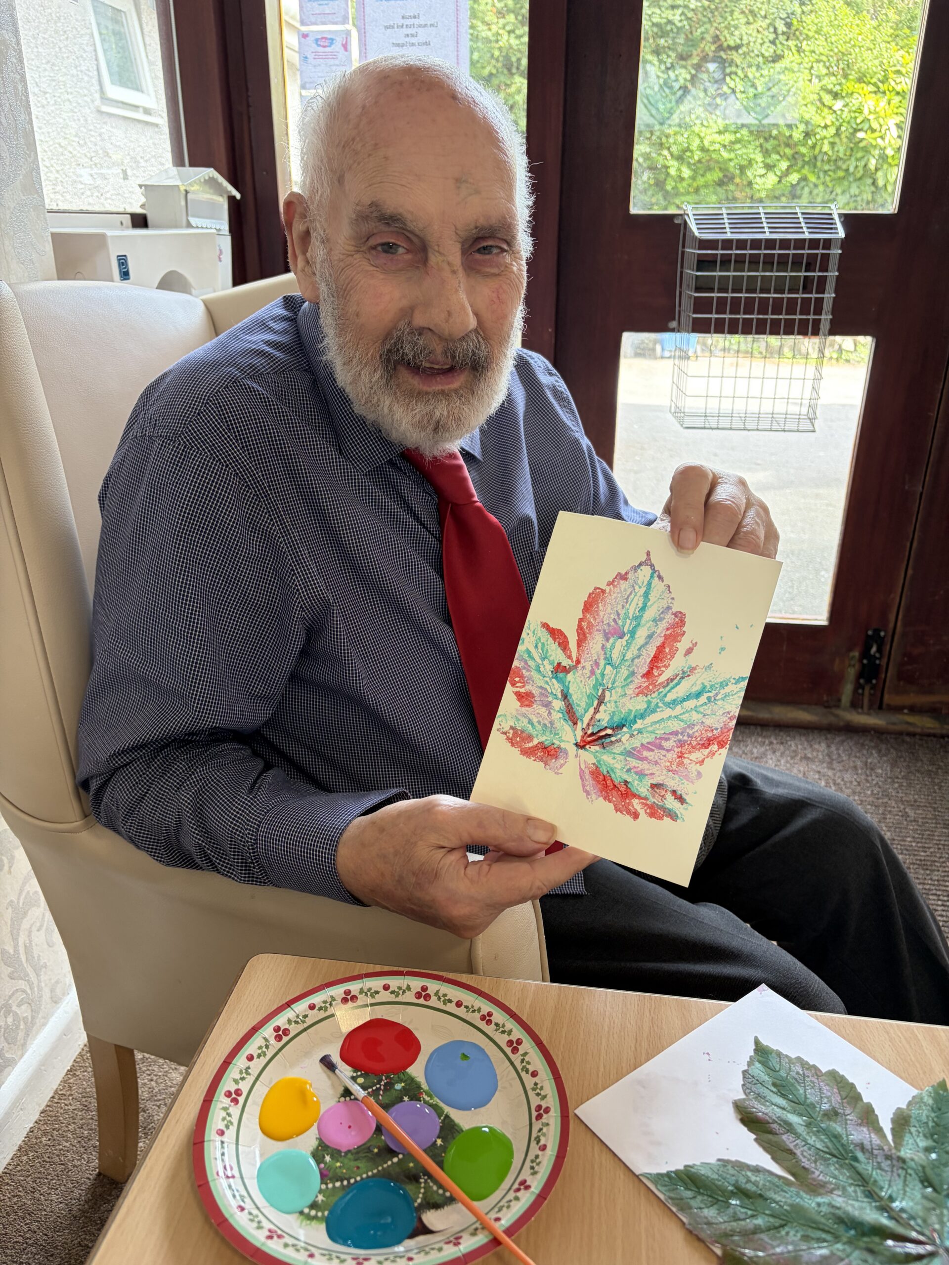 A male resident proudly holding up his finished artwork of a leaf in different coloured paints scaled