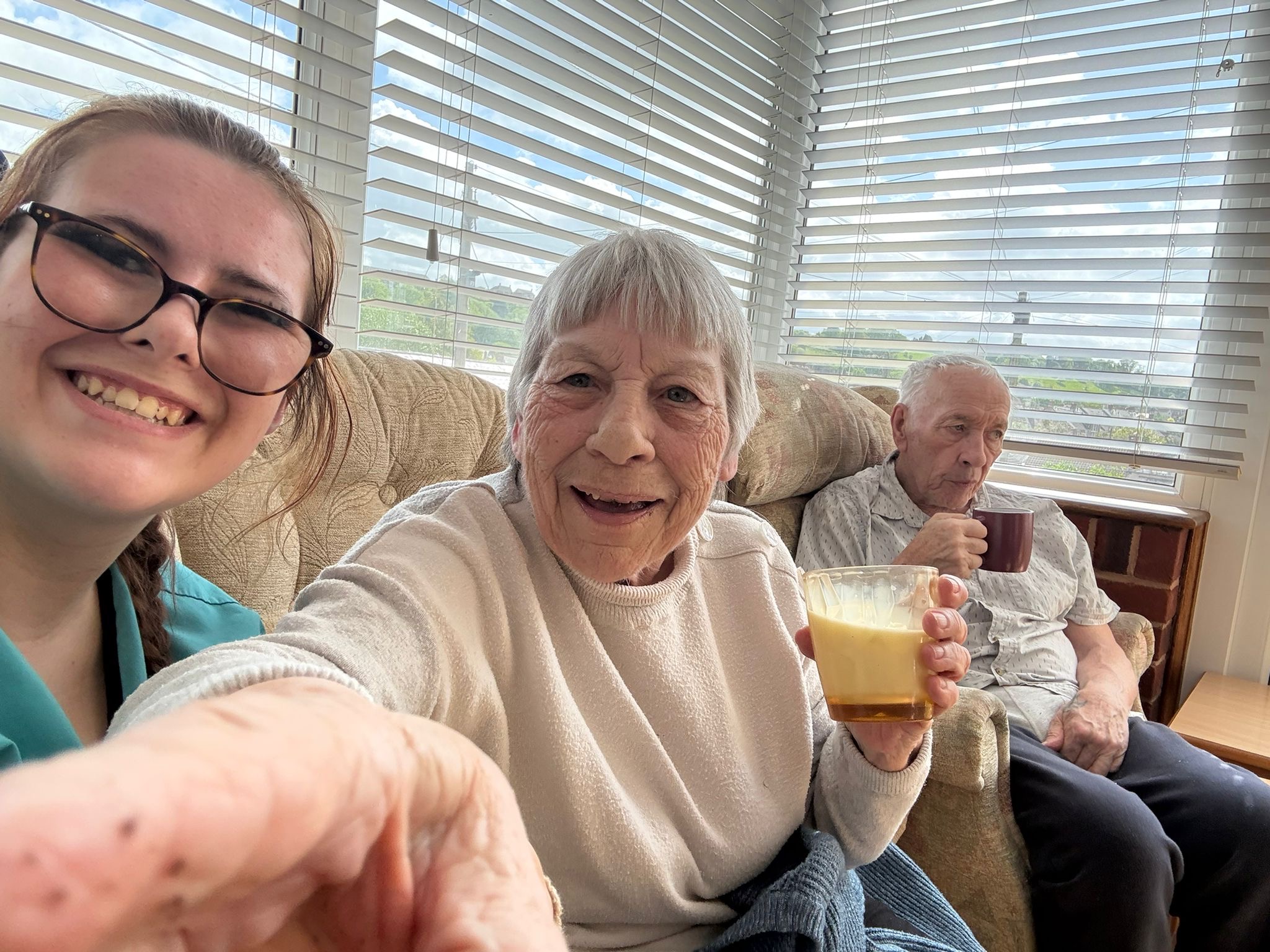 Ange and carer Elly taking a selfie with Bob in the background having drinks