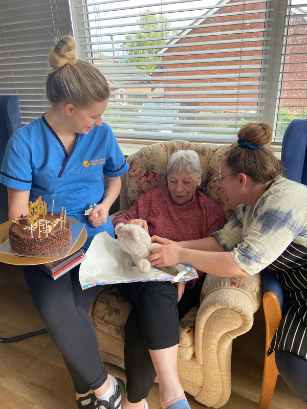 Ange opening a present of a soft toy kitten with Katie seated beside her