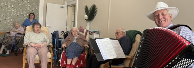 Bing with his accordion and residents seated all smiling