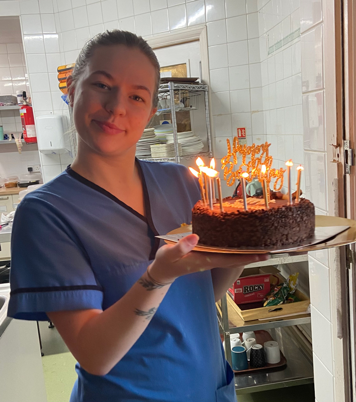 Carer Katie holding a chocolate birthday cake with candles lit