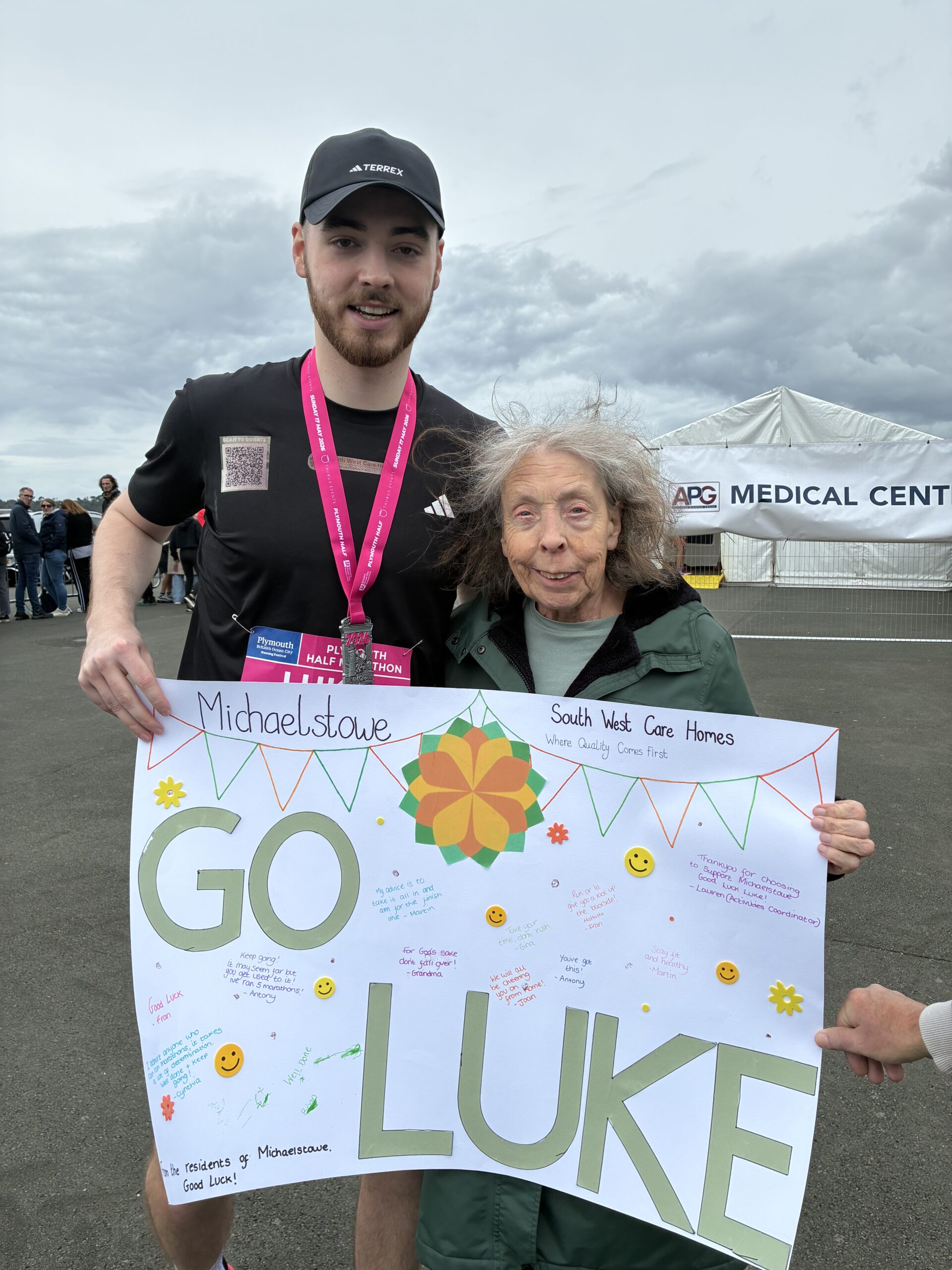 Carol holding her sign with Luke beside her wearing his completion medal scaled