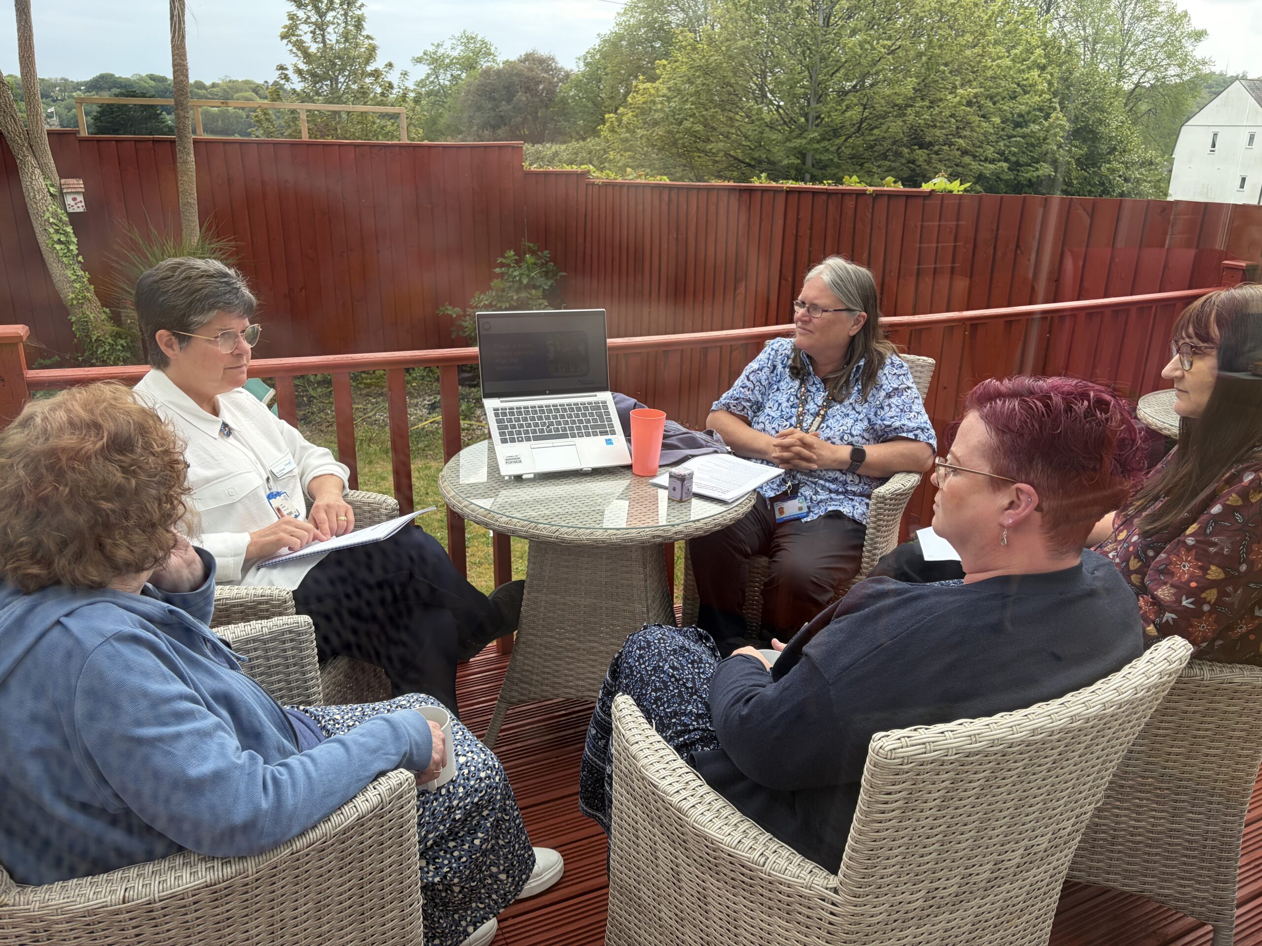 Community nurses seated outside on the decking having a meeting with staff scaled