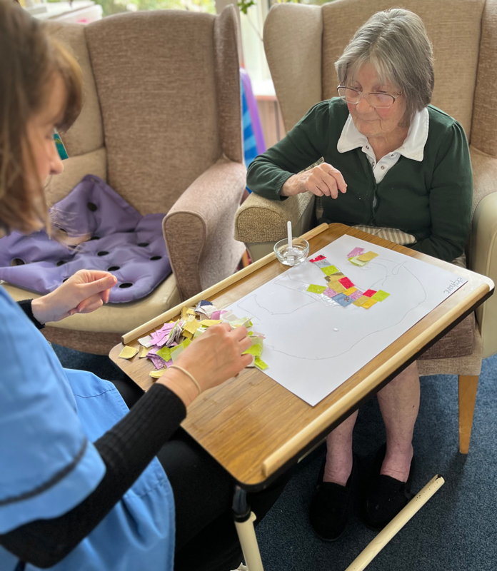 Eileen gluing squares of paper onto an elephant shape