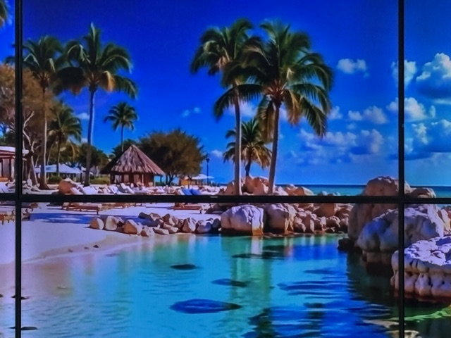 Electronic wall art of a beach with palm trees and wooden huts