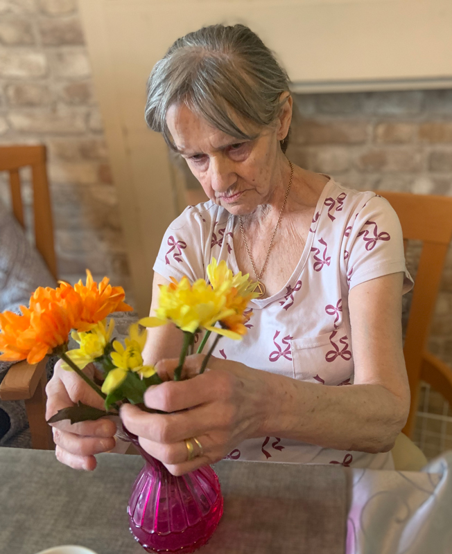 Female resident busy arranging flowers in a pink glass vase