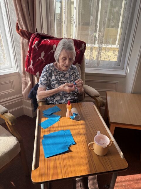 Female resident gluing blue tissue paper to a cardboard tube rotated