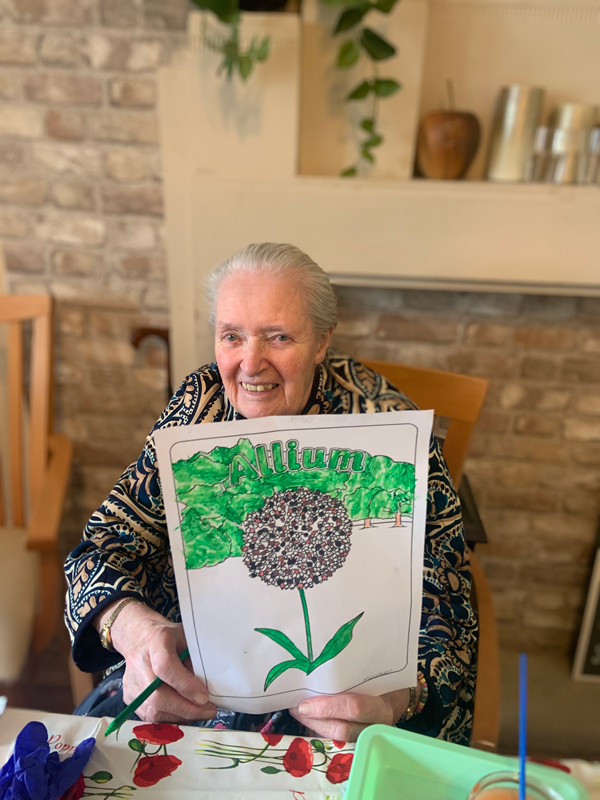 Female resident proudly holding up her finished picture of an Allium smiling