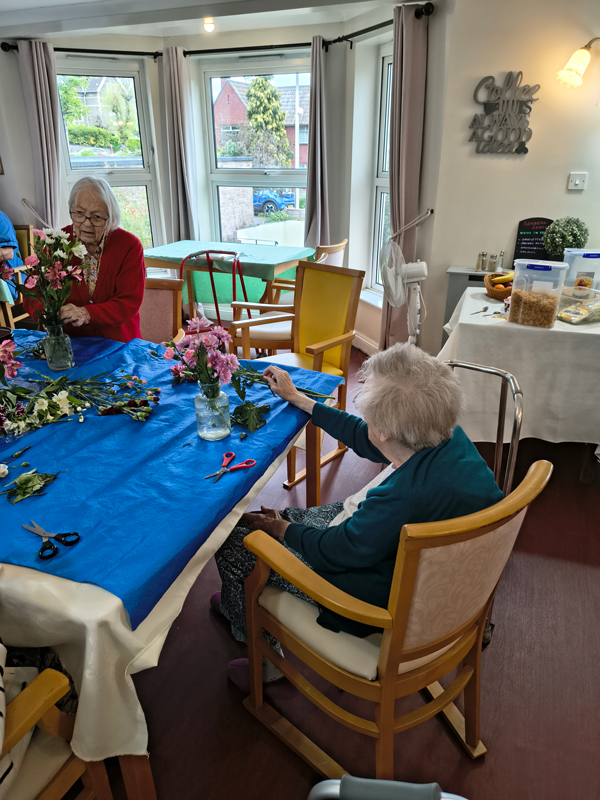 Female resident putting pale pink flowers into a vase