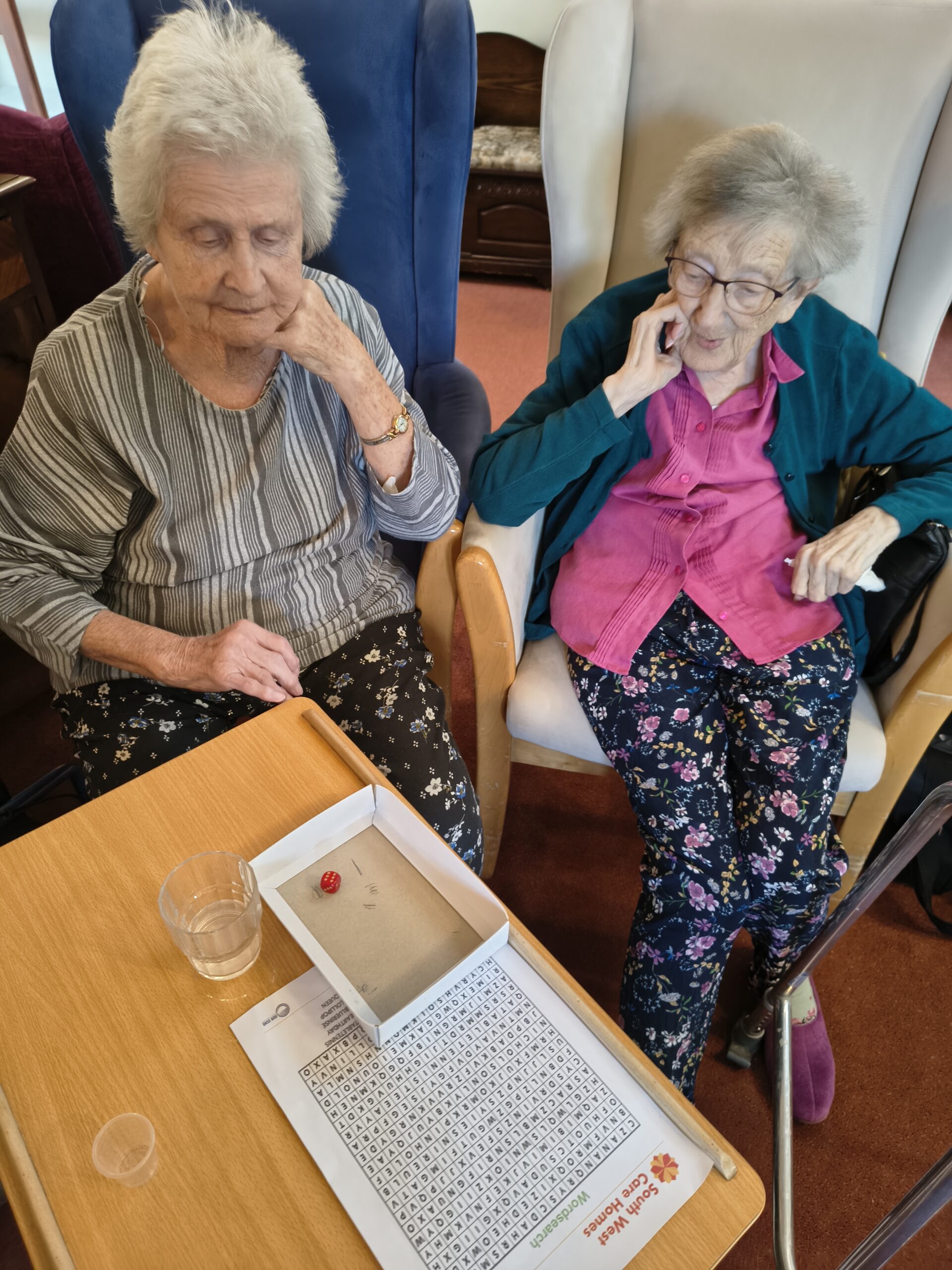 Female resident rolling a die in a box for the duck race with another resident watching scaled