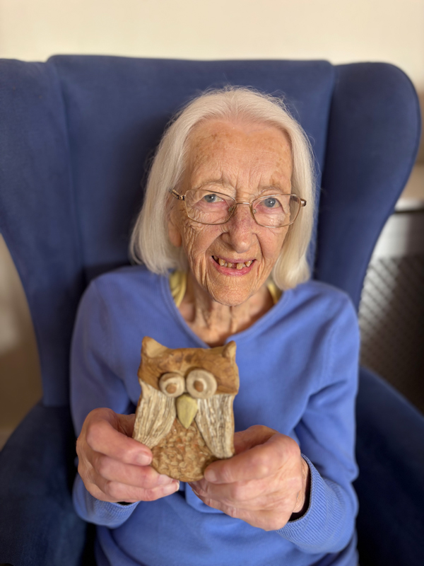 Female resident seated and smiling holding up her pottery owl