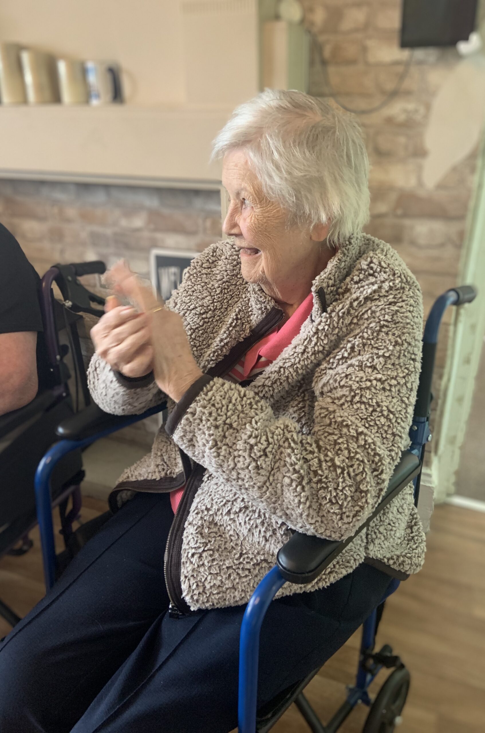 Female resident seated clapping along to the music and smiling scaled