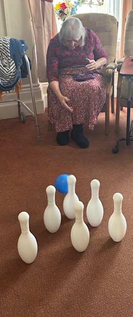 Female resident seated throwing bowling ball at pins