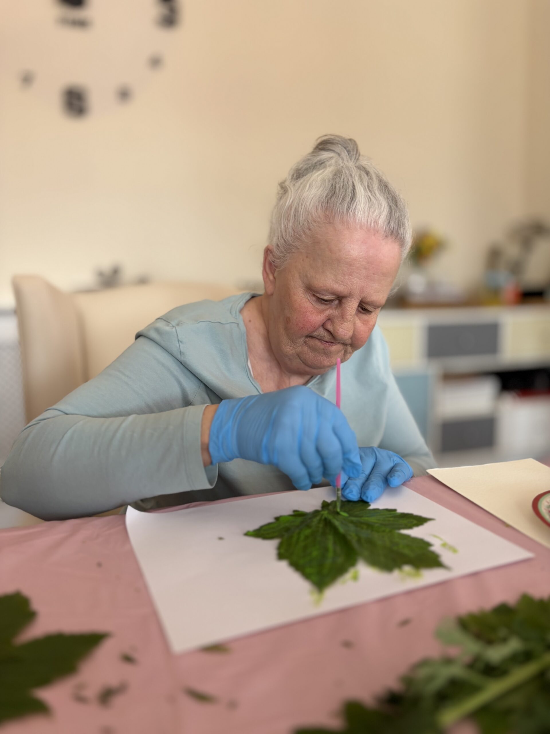 Female resident seated using yellow paint to create her leaf artwork scaled