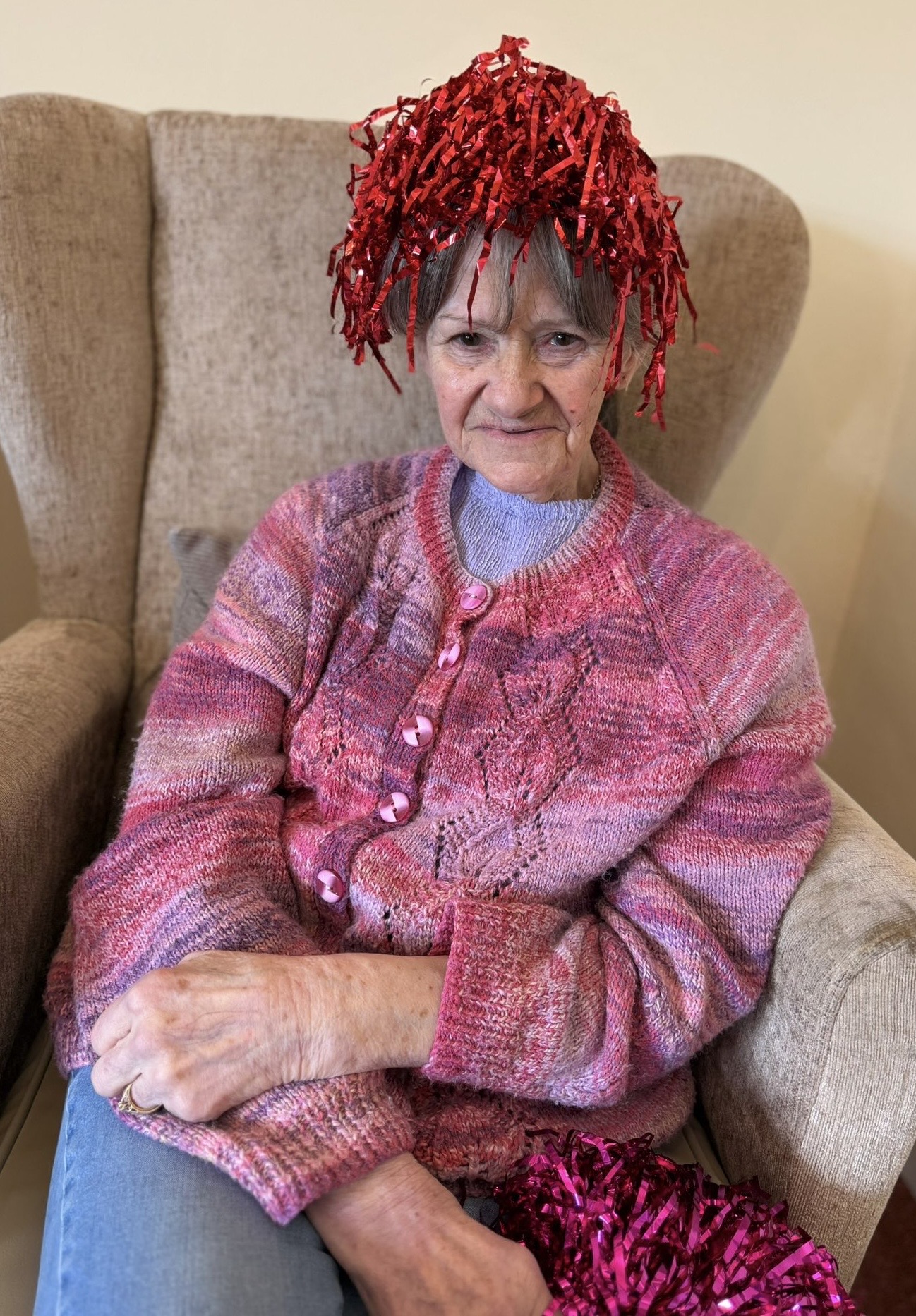 Female resident seated with a red shiny pompom on her head smiling