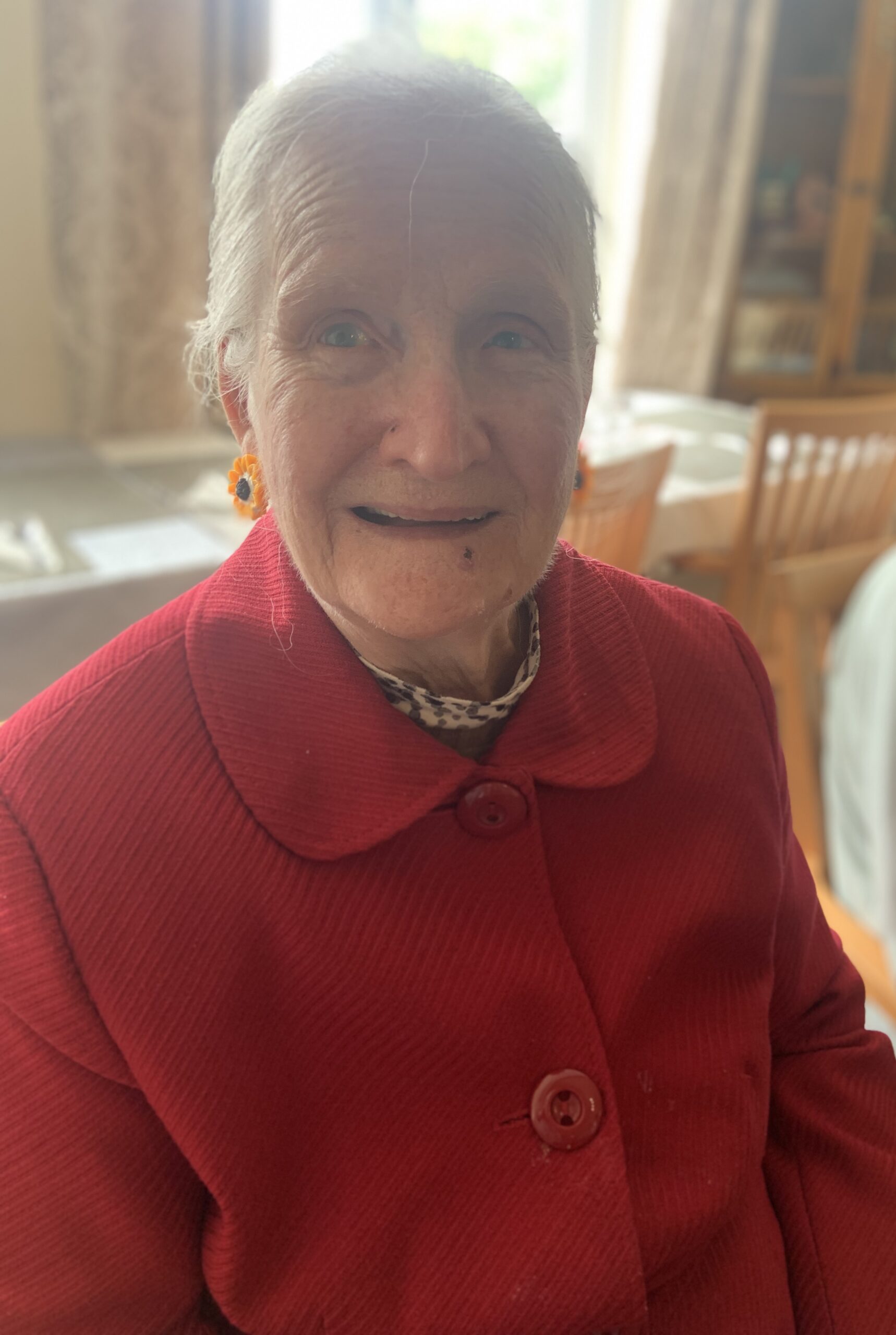 Female resident wearing a red jacket and colourful earrings smiling for the camera scaled