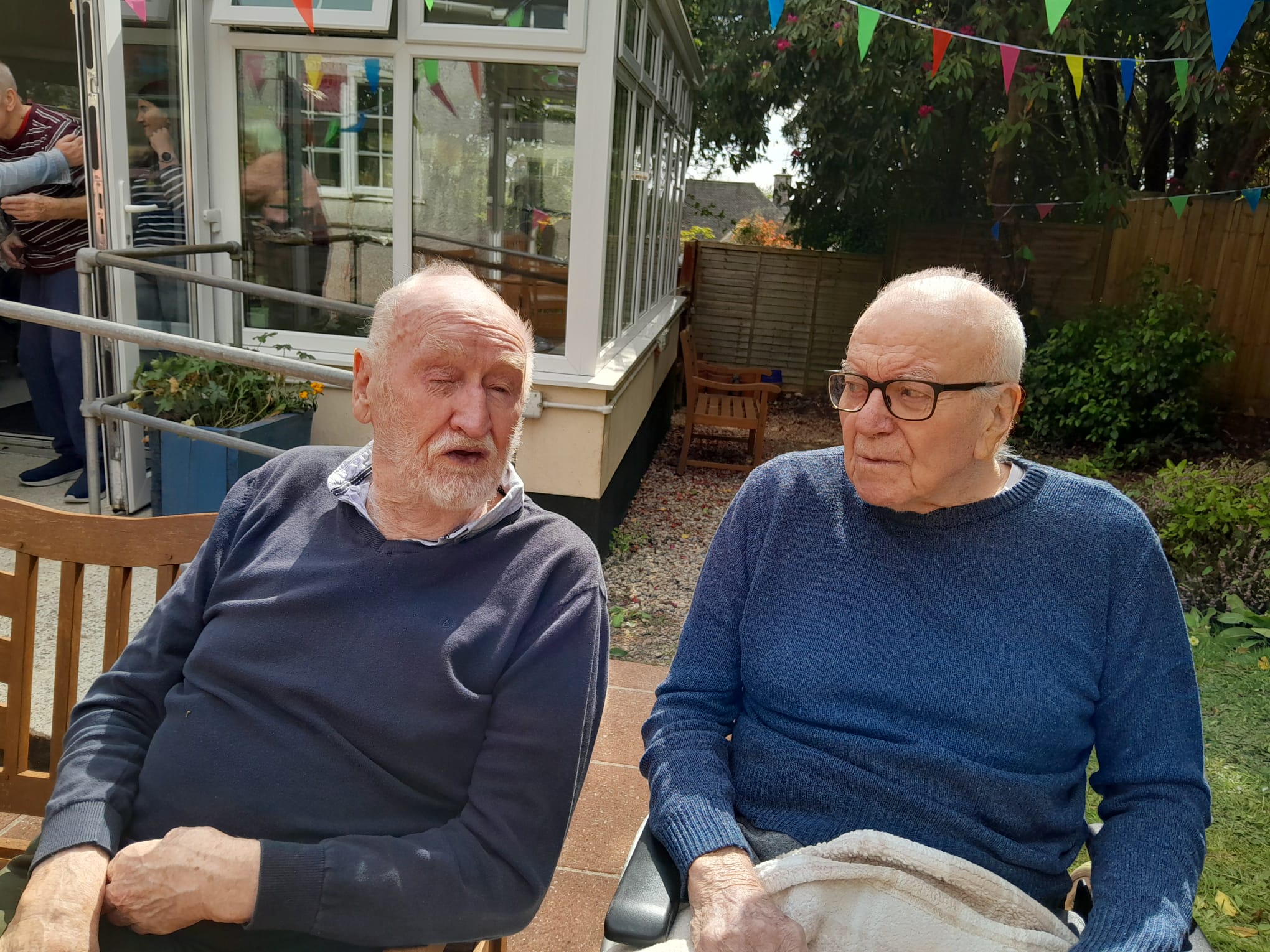 Ivor and Ken seated on a bench and deckchair outside in the sun