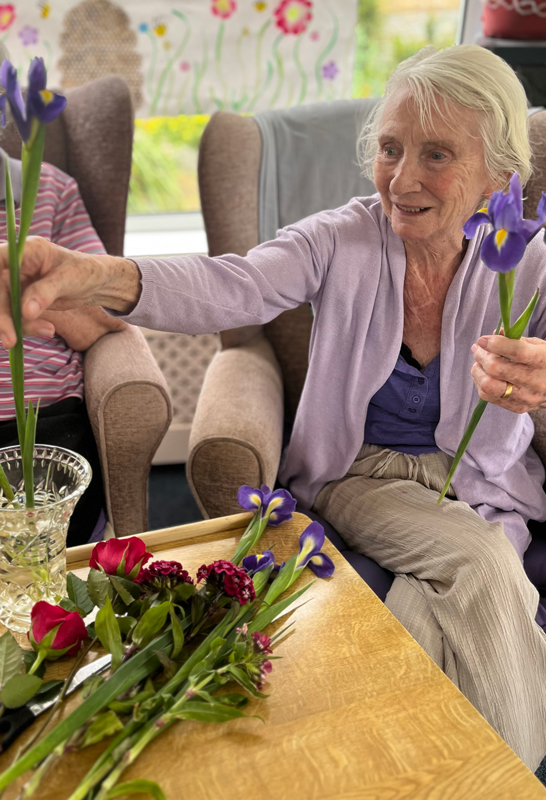 Jean placing purple flowers in a vase