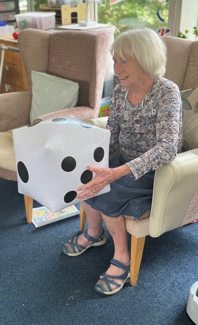 Jean seated holding a large blow-up dice smiling Jean seated holding a large blow up dice smiling