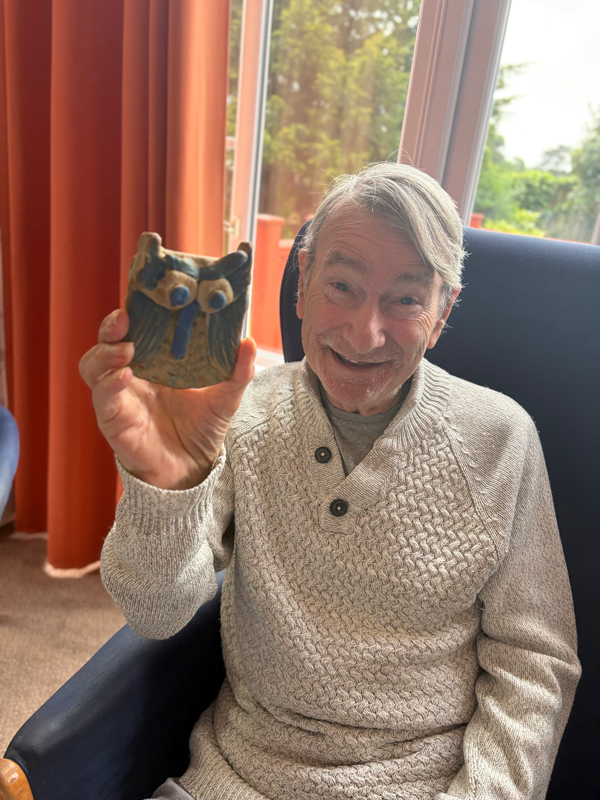 Male resident holding up his finished pottery owl smiling