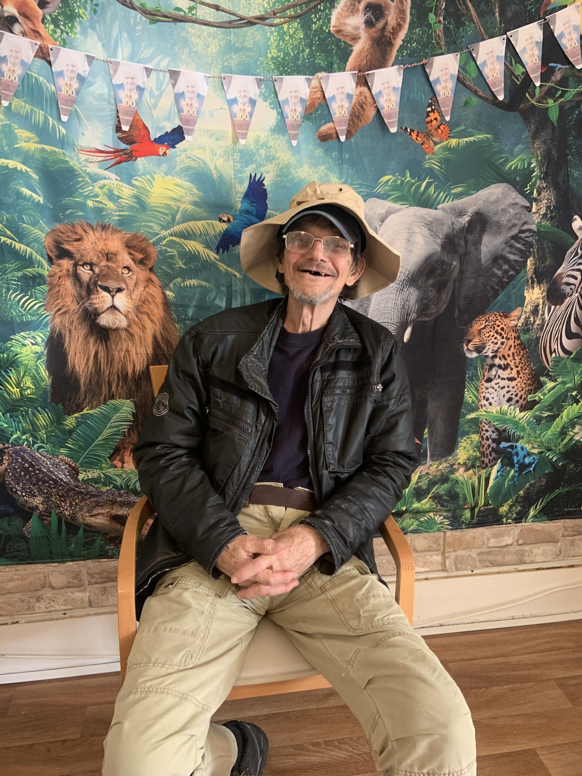 Male resident in a safari hat seated in front of jungle back drop scaled