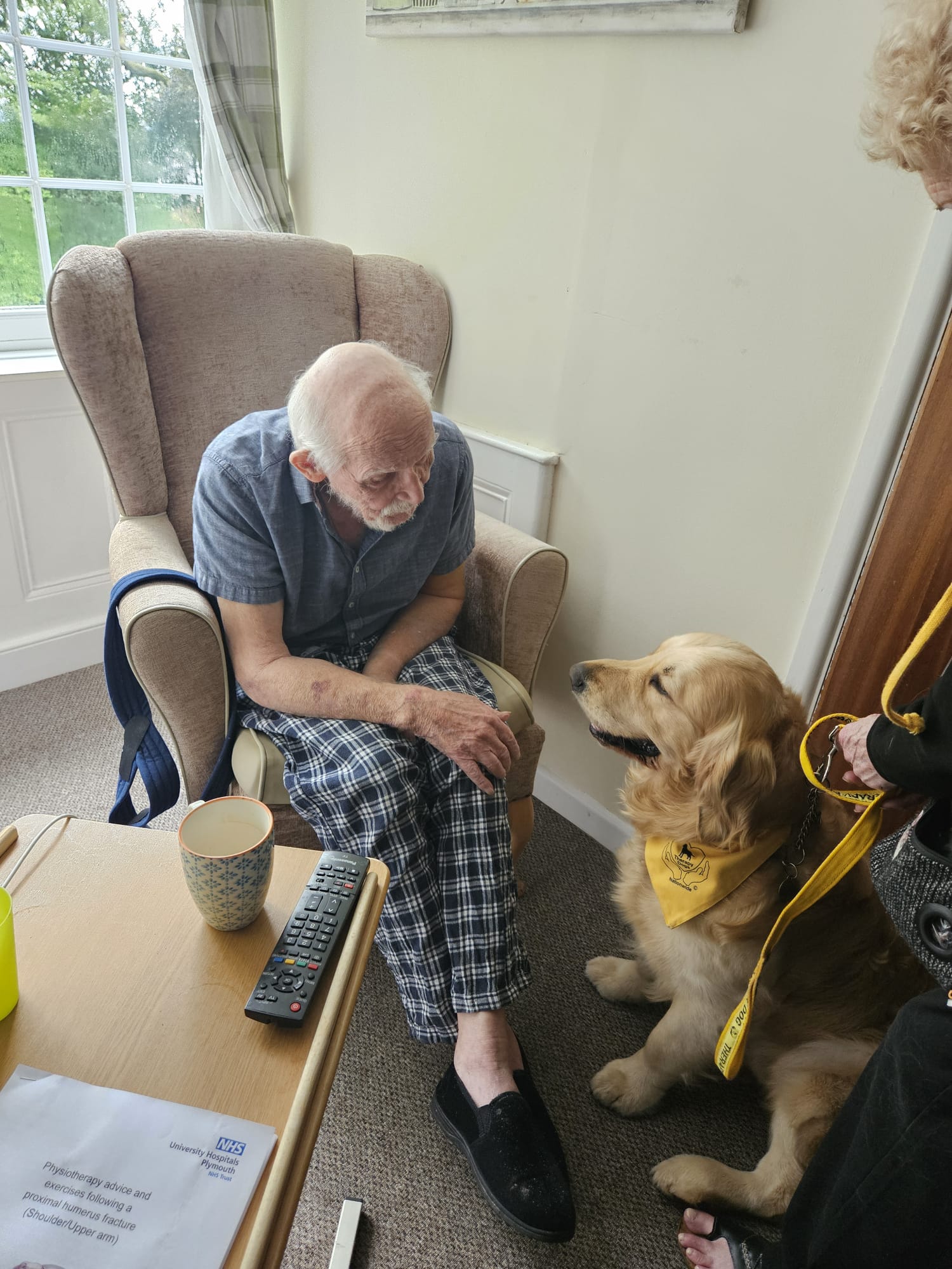 Male resident seated in an armchair Bimble in front of him looking at each other smiling