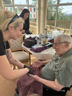 Male resident seated in the conservatory having a hand massage from a student rotated