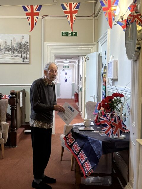 Male resident standing at a table of WW2 memorabilia smiling rotated