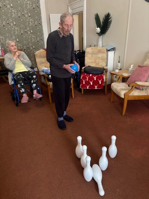 Male resident standing with blue plastic bowling ball looking at the pins rotated