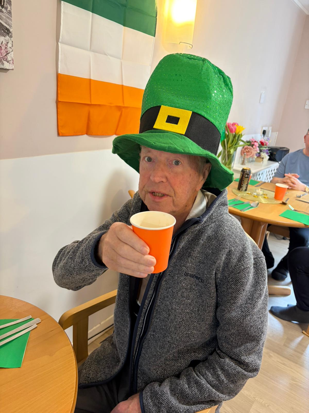 Male resident wearing a leprechaun hat and raising his cup of Guinness