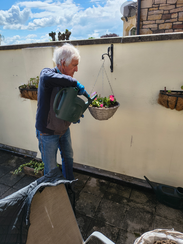 Male watering planted hanging baskets with a watering can