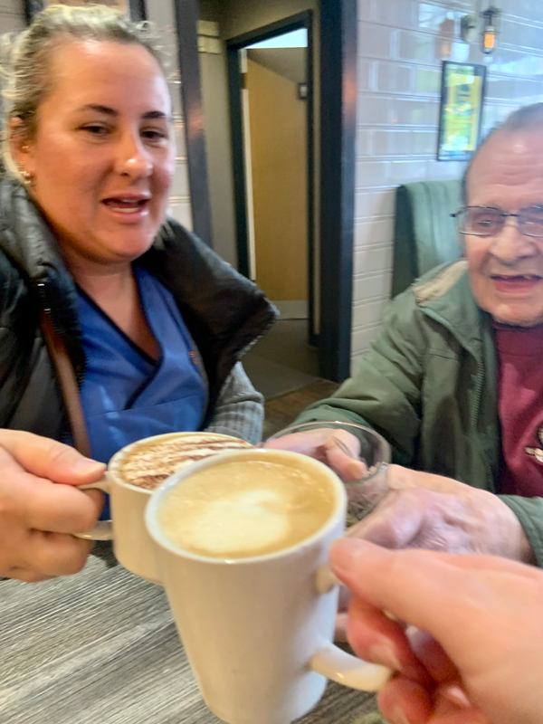 Maurice and carer at a table in the pub clinking coffee cups and glasses