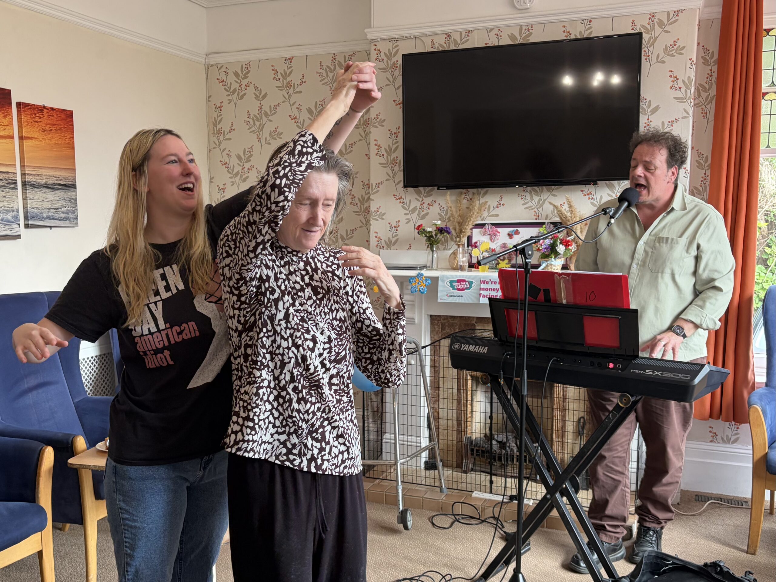 Resident and carer dancing with a man playing the keyboard and singing in the background scaled