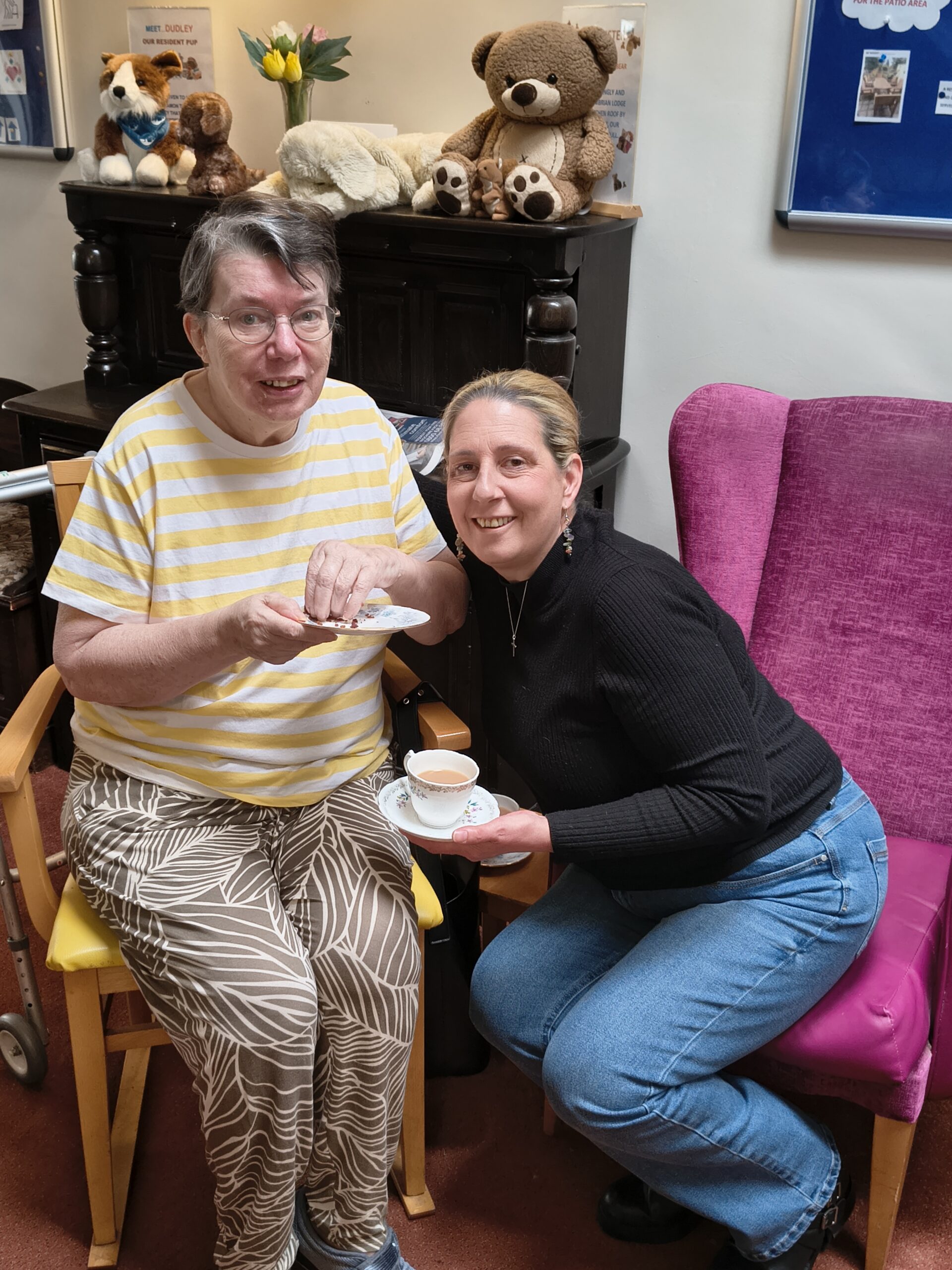 Resident and family member seated with tea and cake smiling scaled