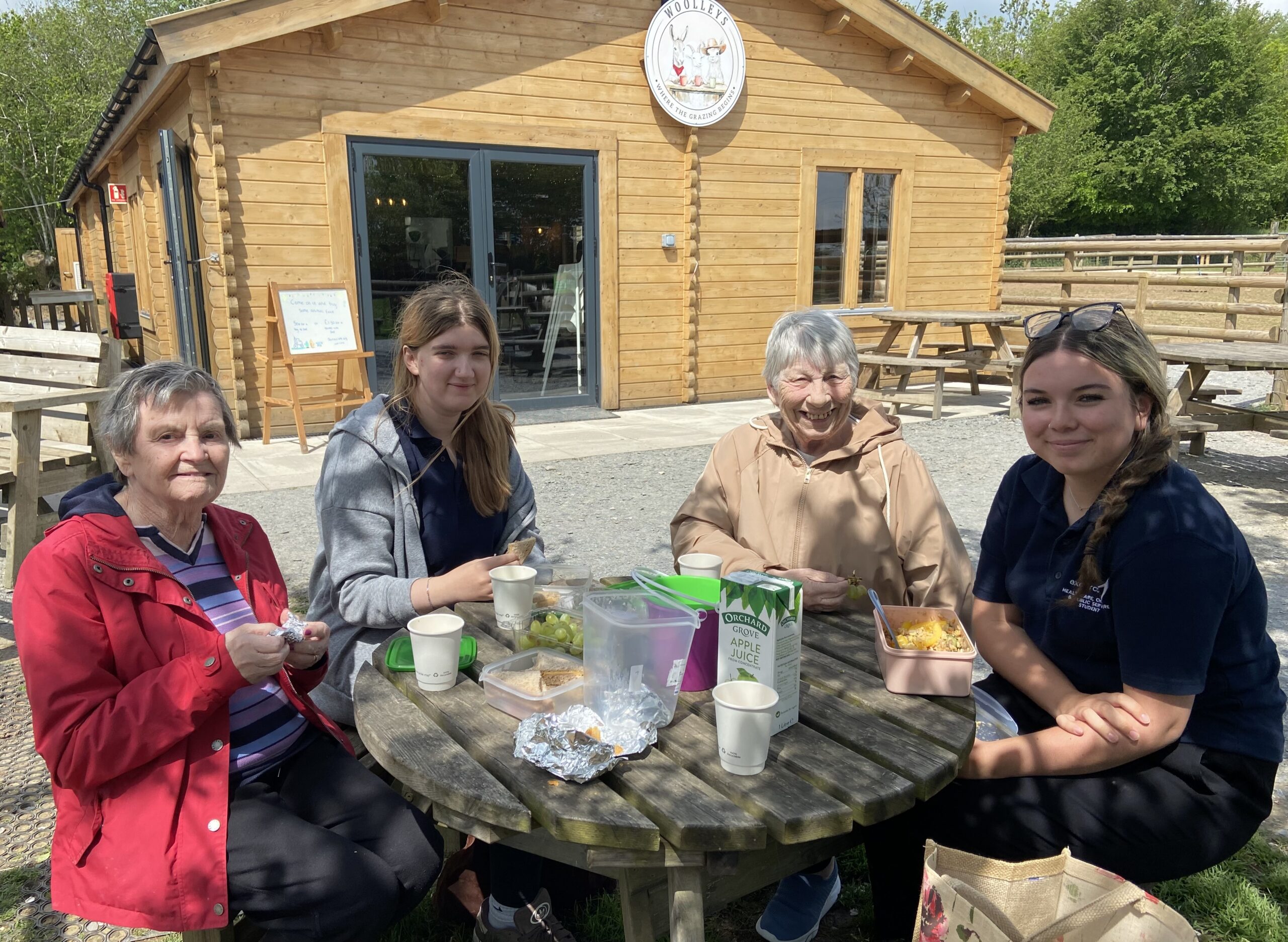 Residents Marj and Ange with carer Amber and one other seated around a picnic table having lunch scaled