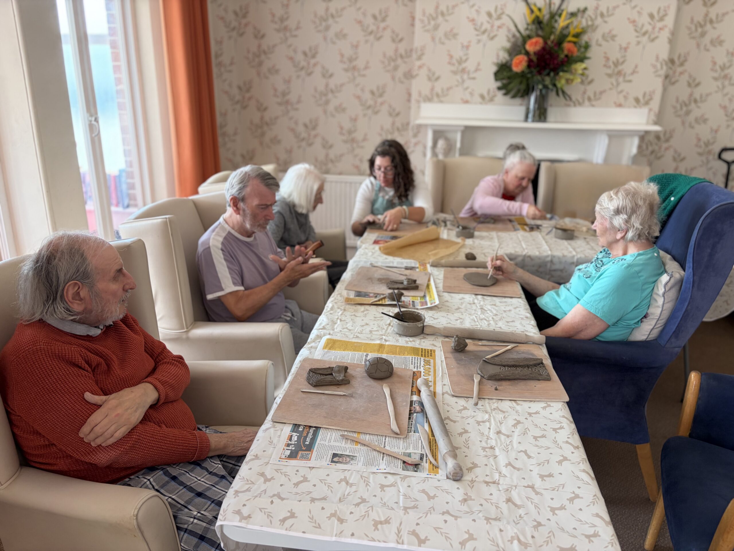 Residents and Rachael seated around an lshaped tables with clay and tools at the ready scaled