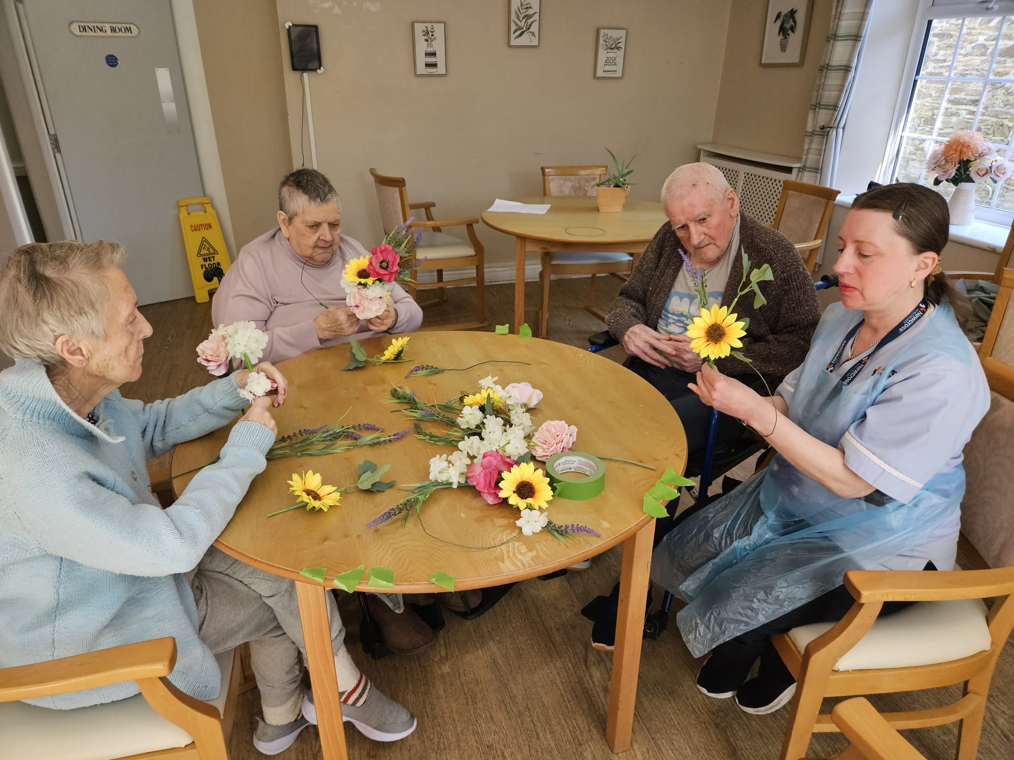 Residents and carers seated around a table together making flower wreaths