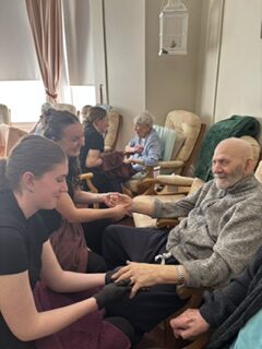Residents seated in armchairs receiving hand massages from college students rotated