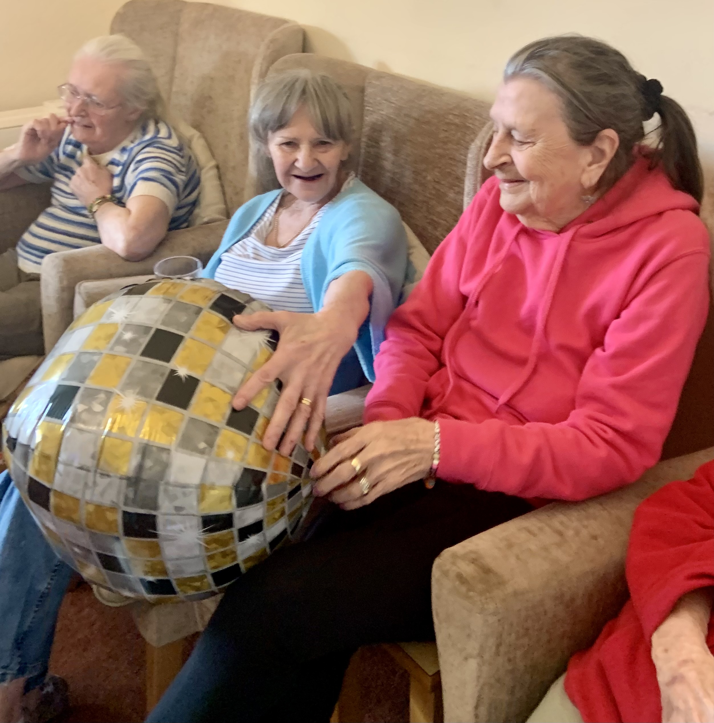 Residents seated in armchairs talking holding a large balloon