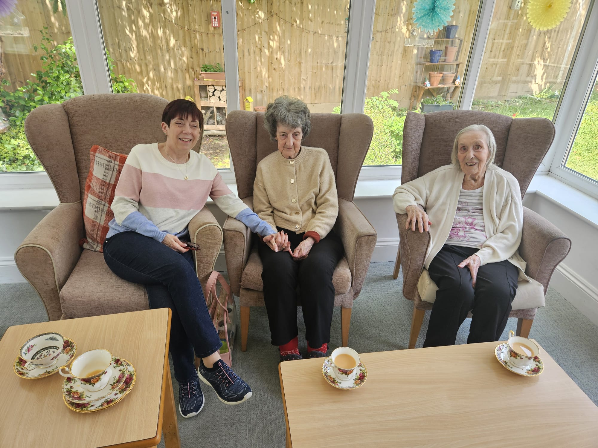 Residents seated in comfy armchairs in the conservatory with their tea